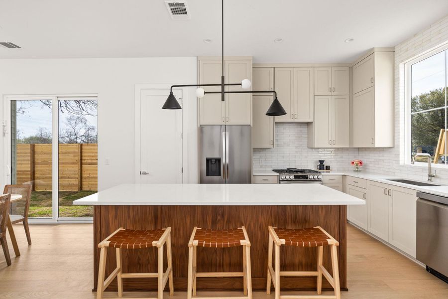 Kitchen featuring a kitchen island, a breakfast bar, stainless steel appliances, light wood finished floors, and decorative backsplash Kitchen featuring a kitchen island, a breakfast bar, stainless steel appliances, light wood finished floors, and decorative backsplash