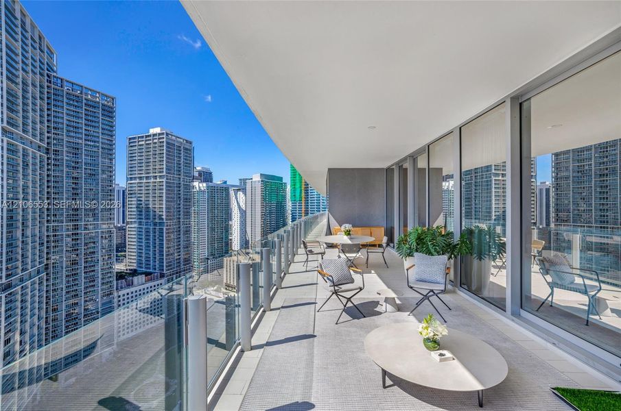 Expansive covered balcony featuring glass panel railings, concrete-finish flooring, and floor-to-ceiling glass wall panels