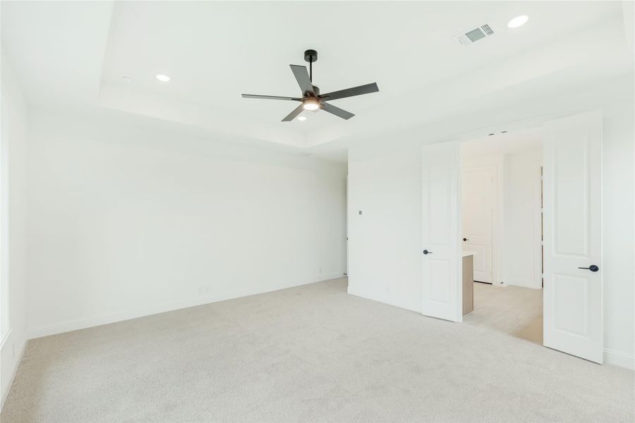 Empty bedroom with tray ceiling, ceiling fan, carpet flooring, and two white doors leading to closet and hallway