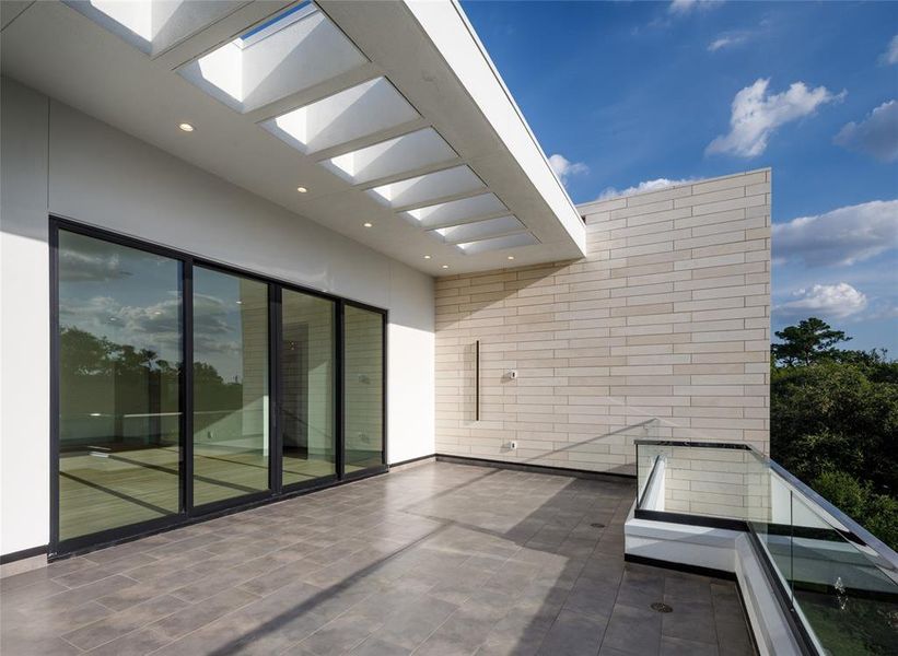 Third floor spacious private terrace off the game room with glass railing, custom cut natural lime stone wall and outdoor wall sconces