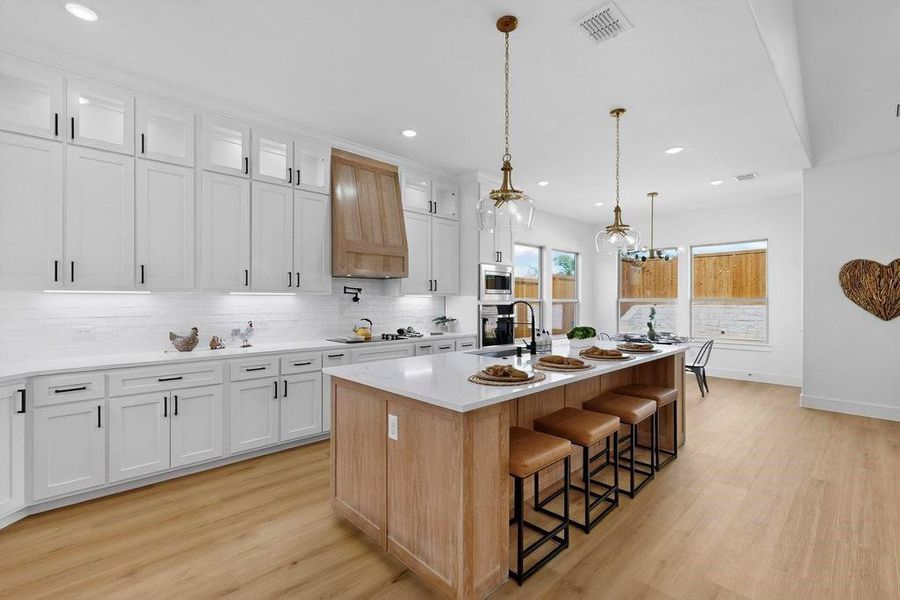 Kitchen featuring decorative backsplash, light wood-style flooring, a kitchen bar, a center island with sink, and recessed lighting