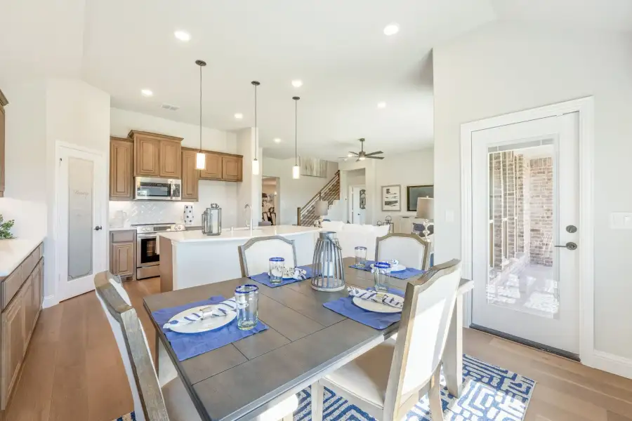 Open-concept dining area with wood table and blue place settings, open to kitchen with brown cabinets and white island