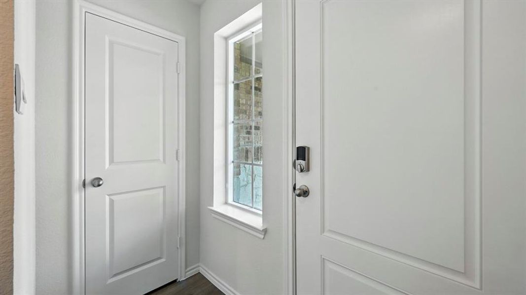 Entryway featuring a panel door with smart lock, an additional panel door, a window with exterior brick detail, and wood-finish flooring Entryway featuring a panel door with smart lock, an additional panel door, a window with exterior brick detail, and wood-finish flooring