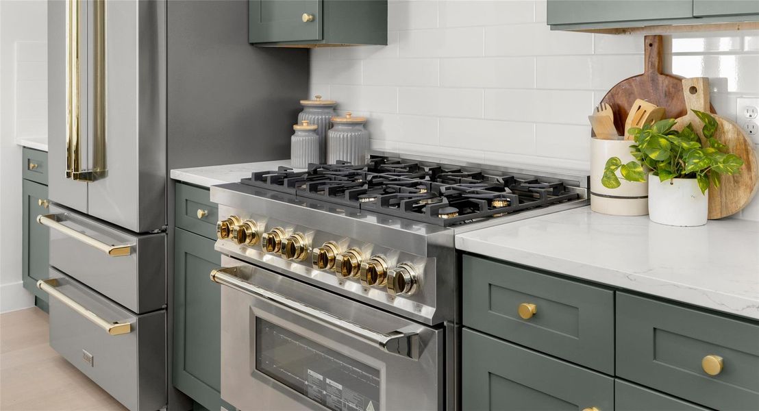 Kitchen with green cabinetry, high end range, light stone counters, and backsplash