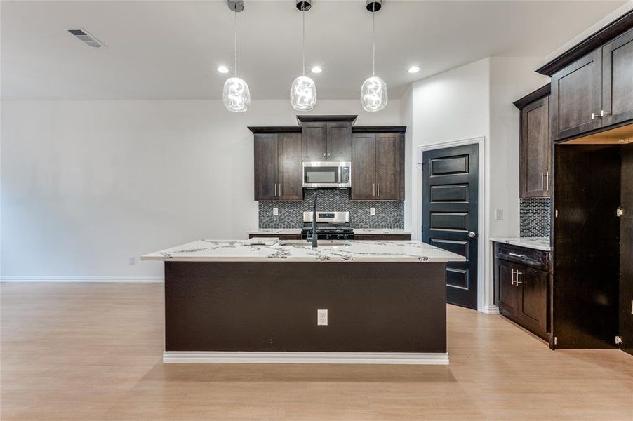 Kitchen with dark brown cabinets, stainless steel appliances, decorative backsplash, and light hardwood / wood-style floors