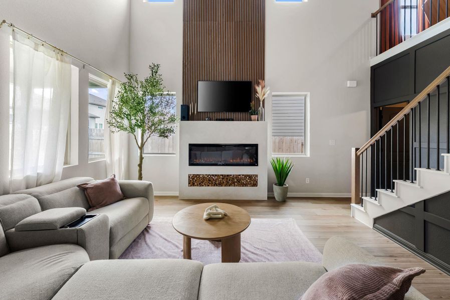 Living room featuring light wood-type flooring, a high ceiling, and a glass covered fireplace