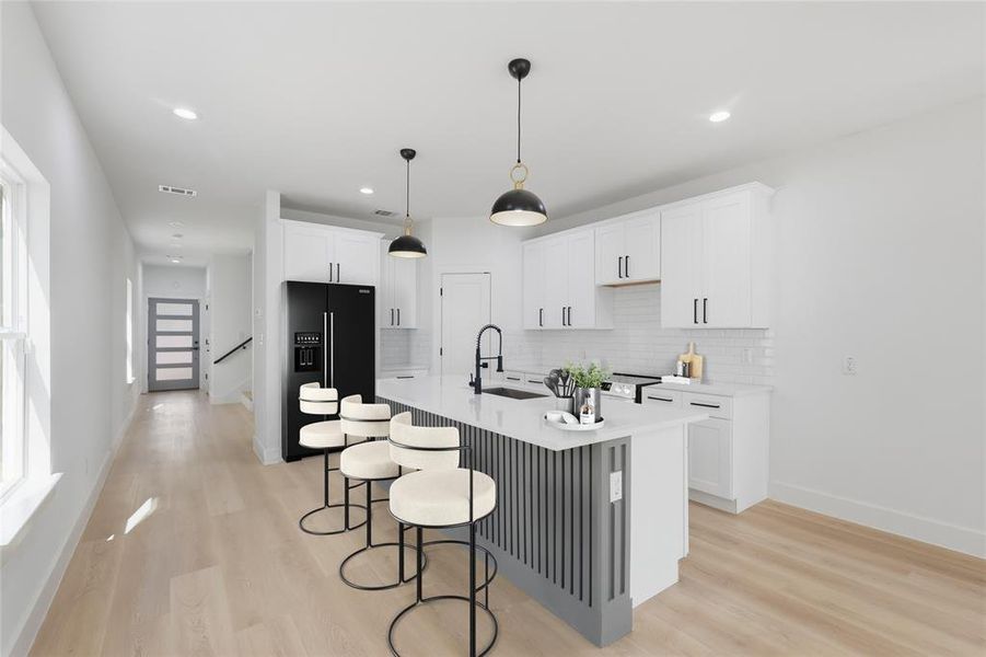 Kitchen with a breakfast bar area, light wood finished floors, white cabinetry, black refrigerator with ice dispenser, and a kitchen island with sink
