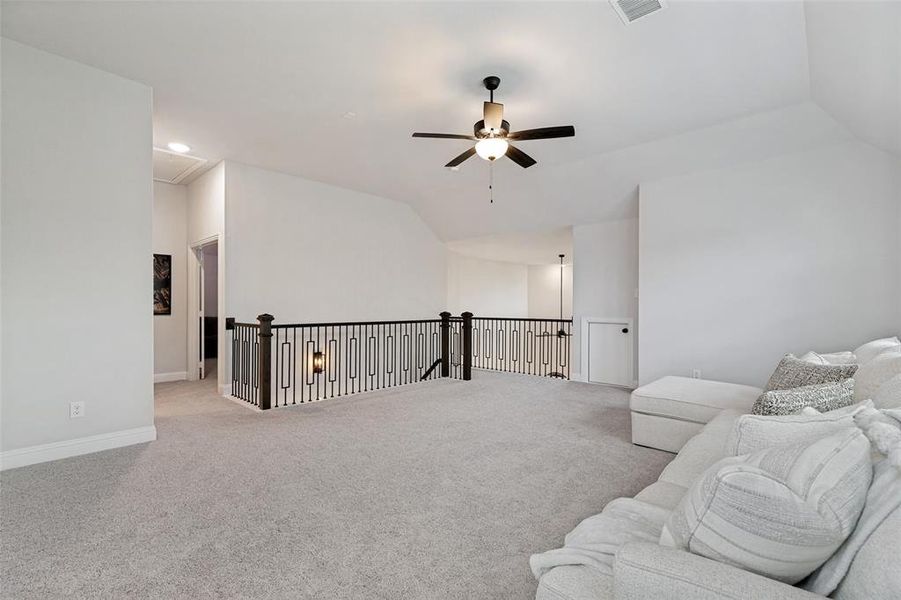 Expansive second-story landing featuring soft carpeting, a decorative metal and wood railing, and a ceiling fan with integrated lighting