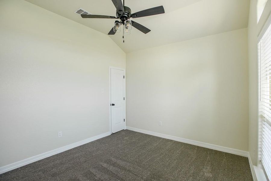 Spare room with dark colored carpet, lofted ceiling, and a ceiling fan Spare room with dark colored carpet, lofted ceiling, and a ceiling fan