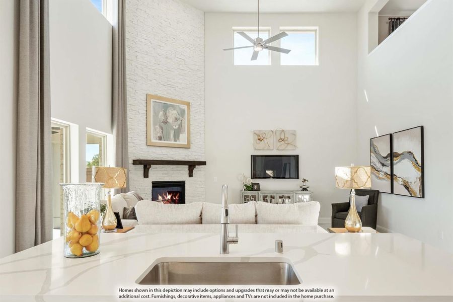 Open-concept living room with two-story white stone fireplace, ceiling fan, and kitchen island in foreground