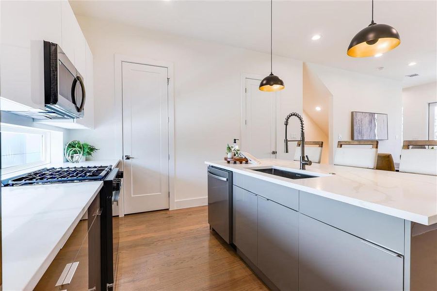 Kitchen featuring dishwasher, hanging light fixtures, sink, black range with gas stovetop, and light wood-type flooring