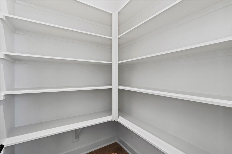 The walk-in pantry features built-in shelving, offering a clean and organized space for all your kitchen essentials.