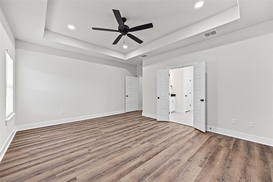 Unfurnished bedroom featuring a tray ceiling, wood finished floors, a ceiling fan, recessed lighting, and connected bathroom Unfurnished bedroom featuring a tray ceiling, wood finished floors, a ceiling fan, recessed lighting, and connected bathroom