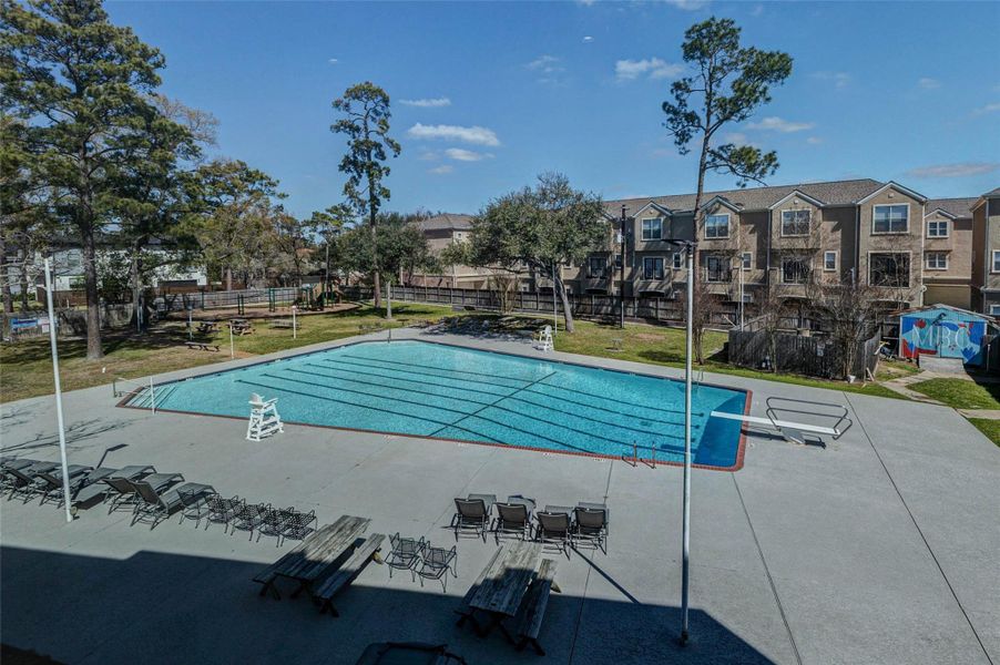 Resort-style community pool within Memorial Townhomes at Verdi, offering expansive deck space, lounge seating, and shaded picnic areas surrounded by mature trees. Clearly marked lap lanes and wide entry steps enhance usability, while the open layout provides ample room for relaxing or social