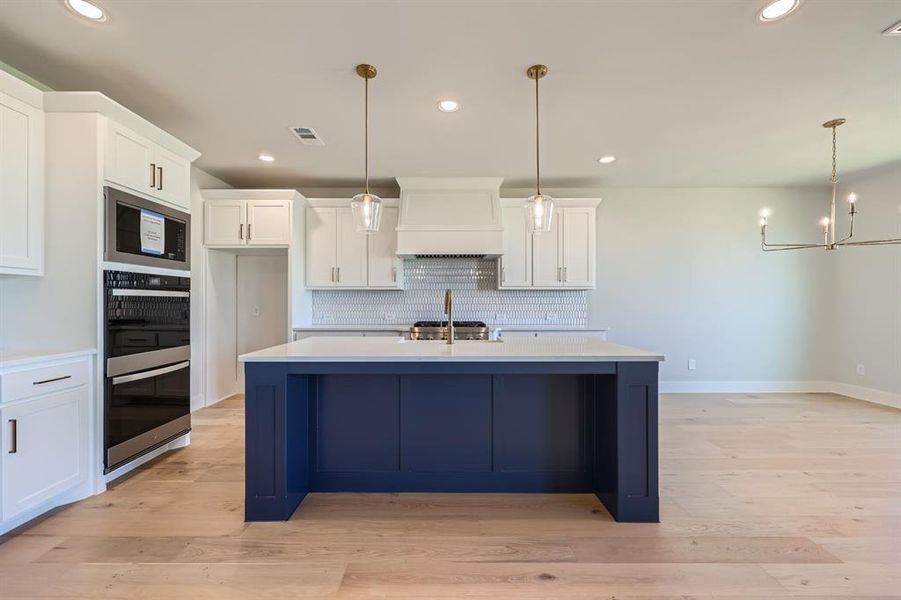 Kitchen featuring pendant lighting, light hardwood / wood-style floors, premium range hood, and a kitchen island with sink