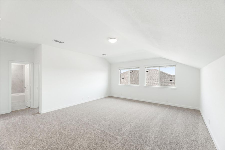 Spacious bedroom with vaulted ceiling, carpet flooring, and attached bathroom doorway