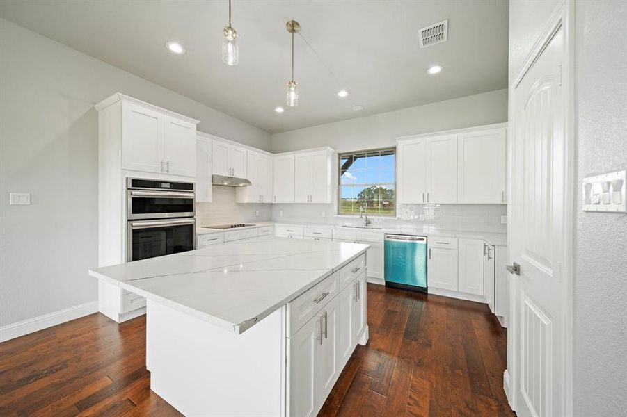 Kitchen with decorative backsplash, dark wood-type flooring, a center island, and appliances with stainless steel finishes