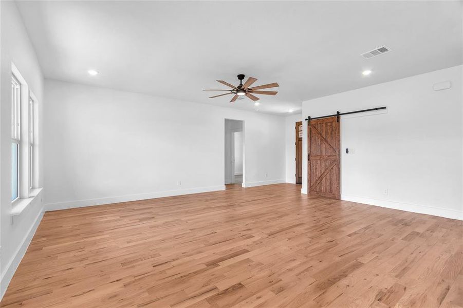 Unfurnished room with ceiling fan, a barn door, and light hardwood / wood-style floors Unfurnished room with ceiling fan, a barn door, and light hardwood / wood-style floors