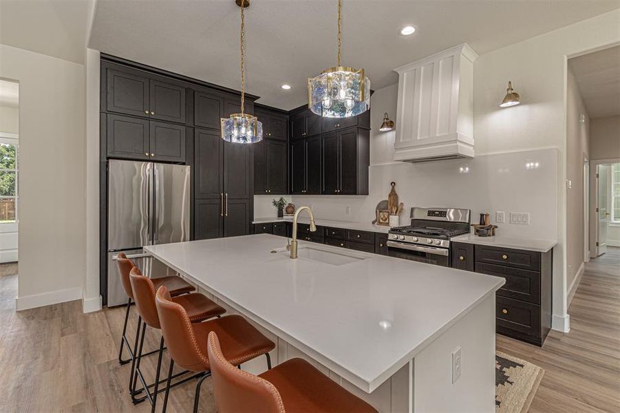 Gourmet kitchen featuring a large central island with seating, dark shaker-style cabinetry, white countertops, stainless steel appliances, and wood-finish flooring