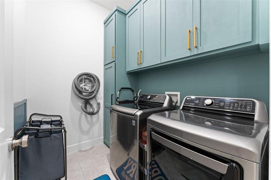 This laundry area features sleek teal cabinetry with gold-toned hardware, providing ample storage