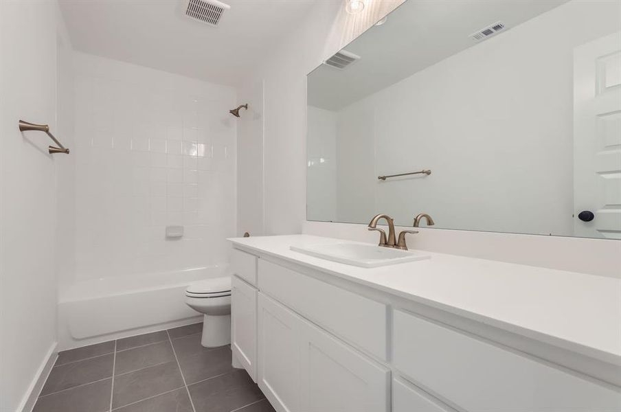 Full bathroom featuring vanity, toilet, tiled shower / bath combo, and tile patterned flooring