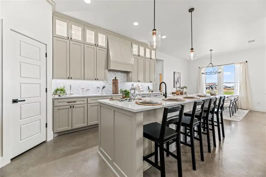 Kitchen with finished concrete flooring, backsplash, custom range hood, an island with sink, and a kitchen bar Kitchen with finished concrete flooring, backsplash, custom range hood, an island with sink, and a kitchen bar