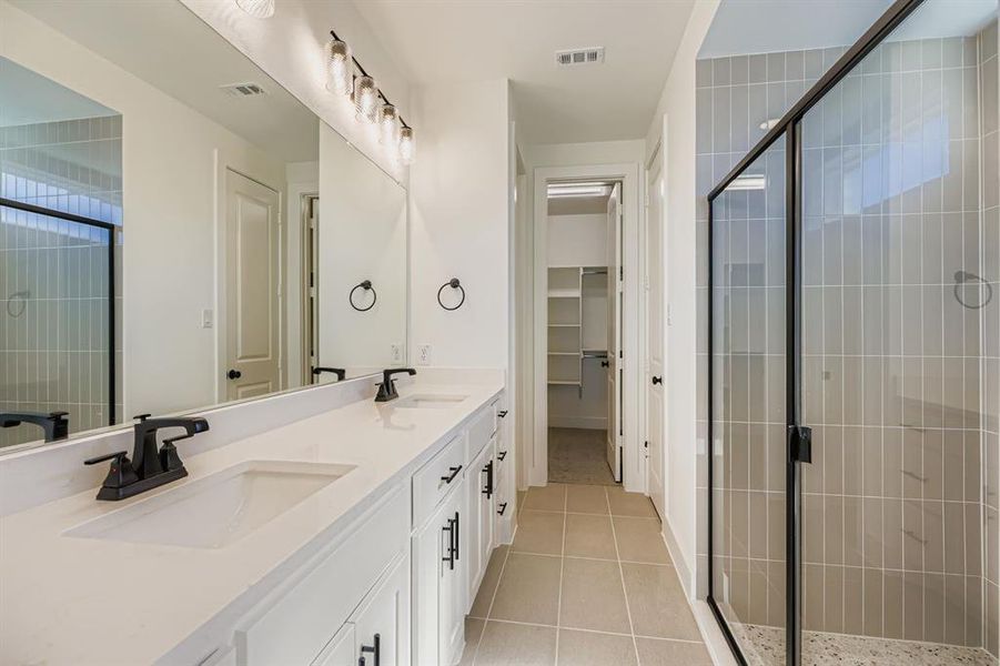 Full bath featuring double vanity, light tile patterned flooring, a stall shower, and a walk in closet Full bath featuring double vanity, light tile patterned flooring, a stall shower, and a walk in closet
