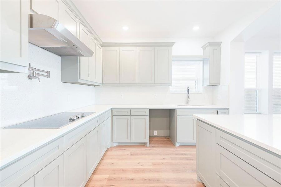 Kitchen featuring light wood finished floors, under cabinet range hood, recessed lighting, black electric stovetop, and light stone countertops
