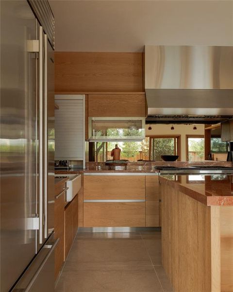 Kitchen featuring modern cabinets, built in refrigerator, wall chimney exhaust hood, light tile patterned flooring, and healthy amount of natural light
