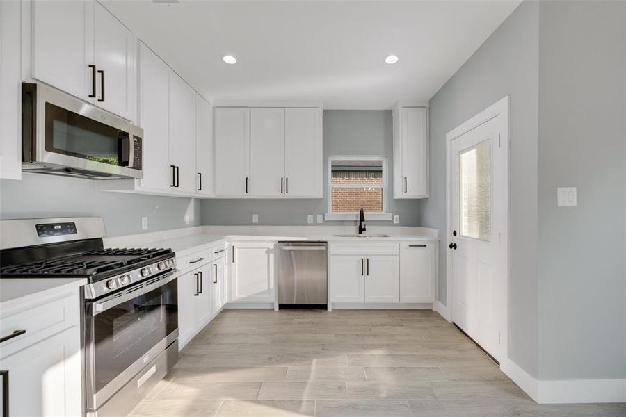 Kitchen with appliances with stainless steel finishes, light hardwood / wood-style flooring, white cabinets, and sink