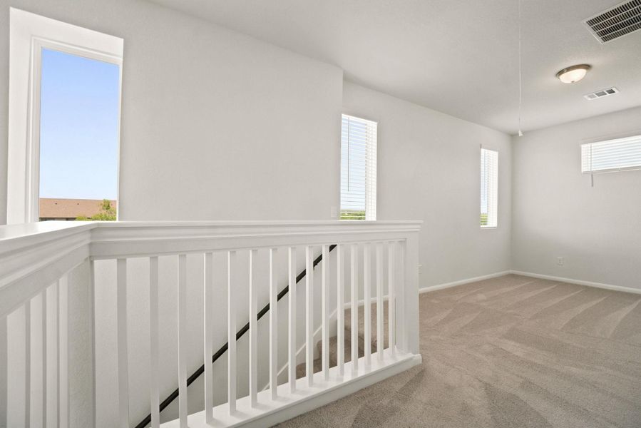An airy upstairs landing displays plush carpeting and multiple windows framing clear sky views.