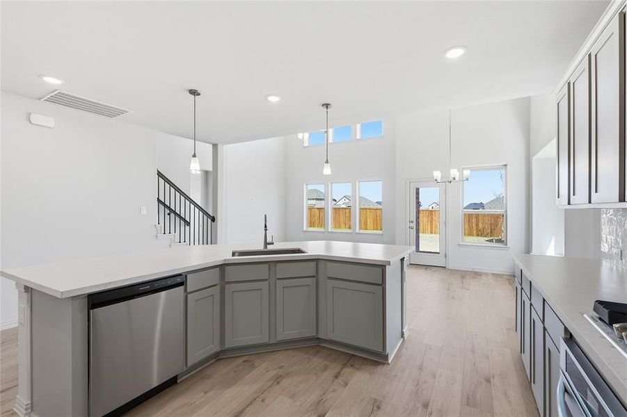 Open-concept kitchen featuring an oversized island with an undermount sink, stainless steel dishwasher, and light-colored countertops