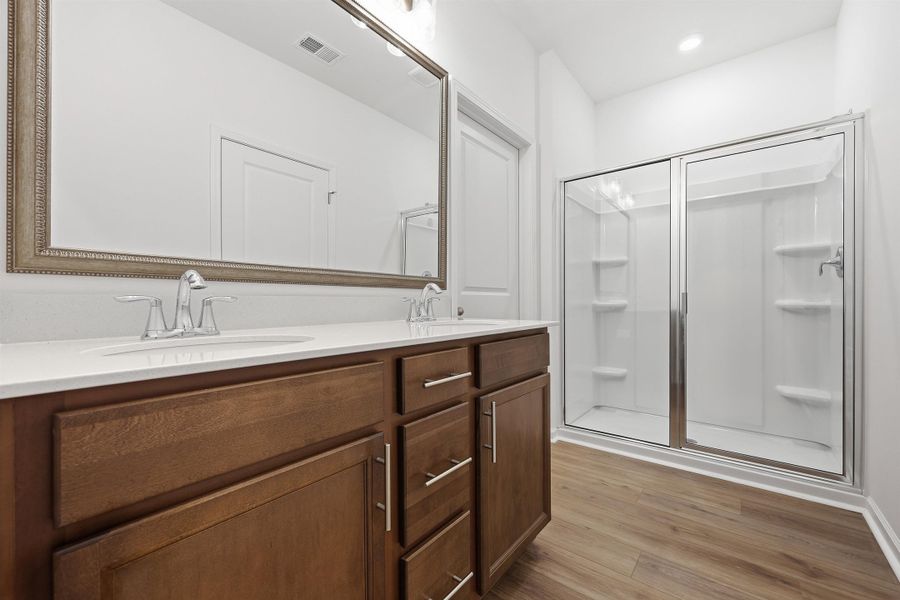 Full bath with light wood-style flooring, double vanity, and a stall shower