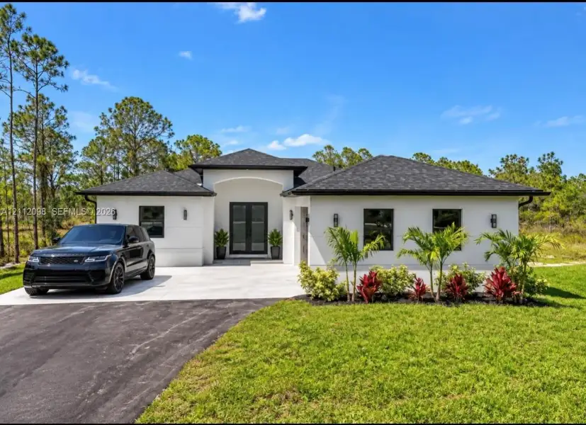 Stucco exterior featuring double glass entry doors, dark window frames, an asphalt shingle roof, and curated landscape plantings Stucco exterior featuring double glass entry doors, dark window frames, an asphalt shingle roof, and curated landscape plantings
