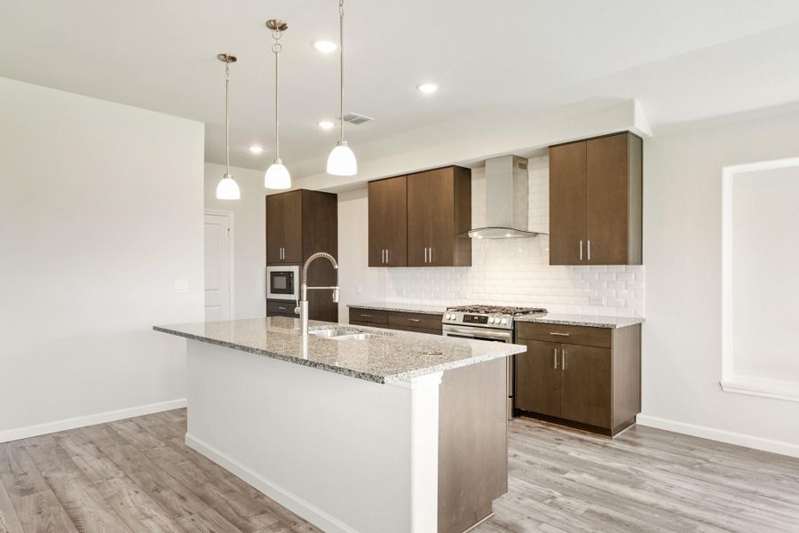 Kitchen with dark wood cabinets, granite island, stainless steel appliances, and pendant lights over hardwood floors