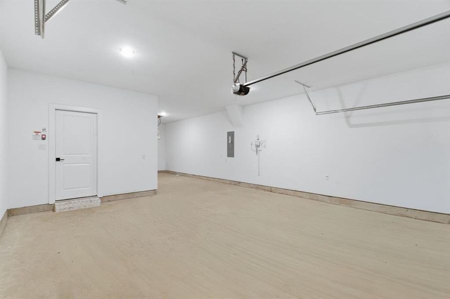 Spacious 3 car garage featuring a light-colored concrete floor, pristine white walls, and an overhead garage door opener mechanism Spacious 3 car garage featuring a light-colored concrete floor, pristine white walls, and an overhead garage door opener mechanism
