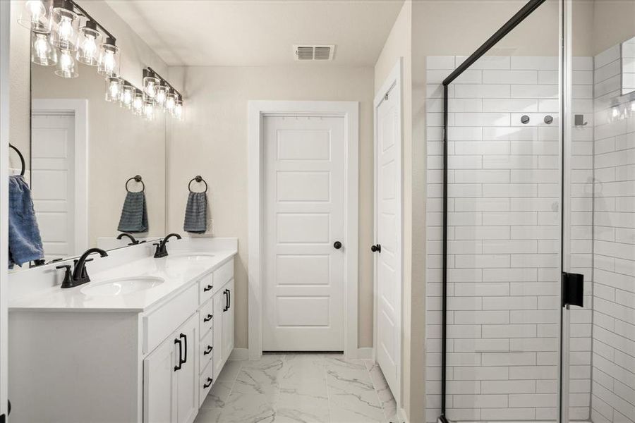Bathroom featuring a stall shower, double vanity, and light marble finish flooring