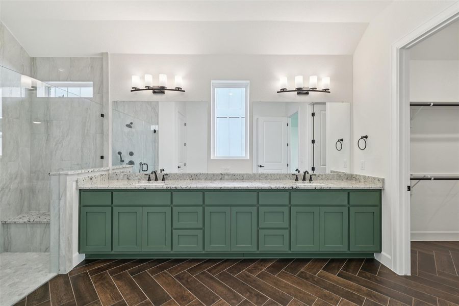 Full bath with a marble finish shower, double vanity, and a walk in closet