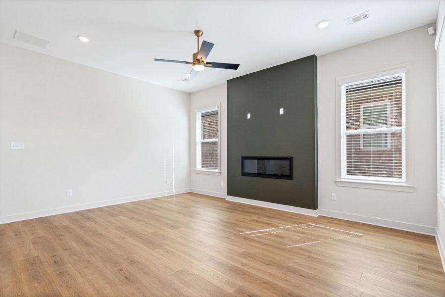Empty room featuring healthy amount of natural light, light wood finished floors, a large fireplace, ceiling fan, and recessed lighting