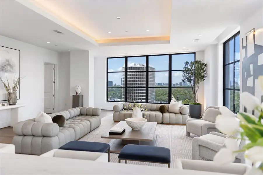 The expansive living room offers an open-concept layout with soaring ceilings, designer finishes, and walls of windows that showcase stunning city and treetop views while filling the space with natural light.