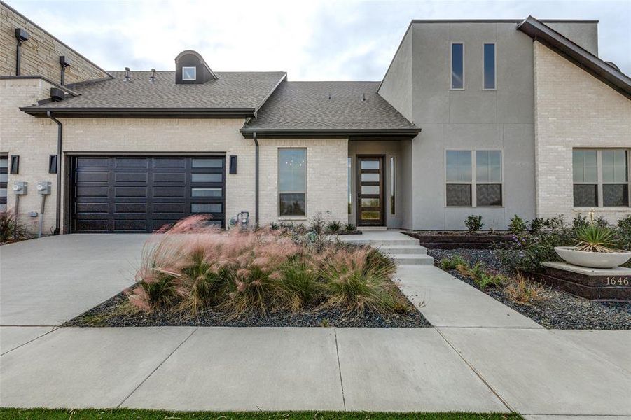 View of front of house featuring brick siding, an attached garage, driveway, and roof with shingles