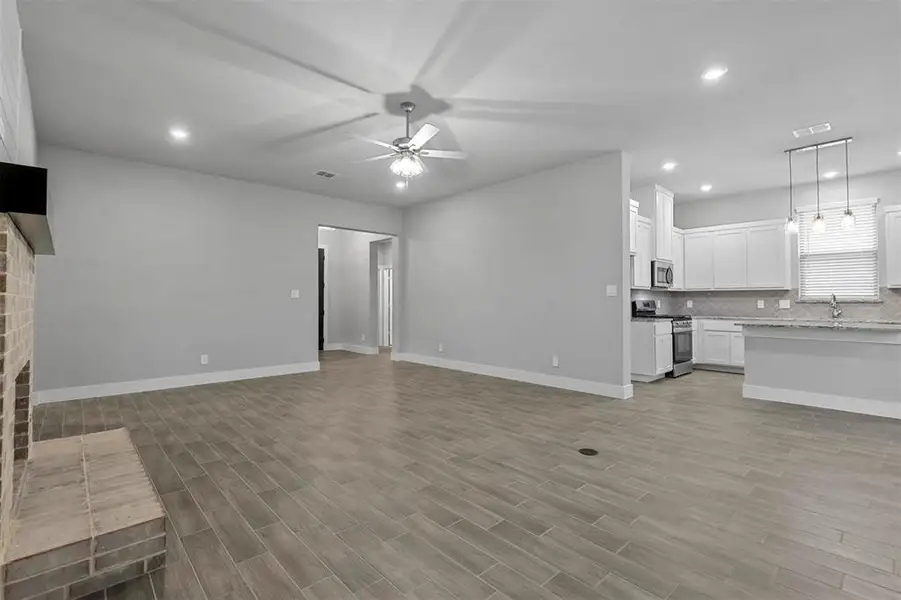 Unfurnished living room with a fireplace, ceiling fan, and light wood-type flooring