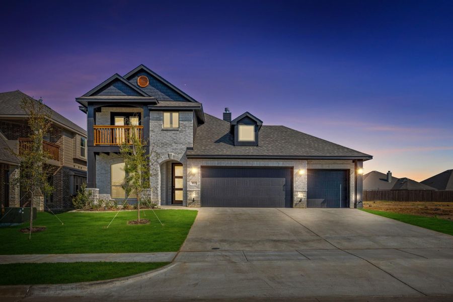 Two-story home with stone exterior, upper balcony, and three-car garage at dusk