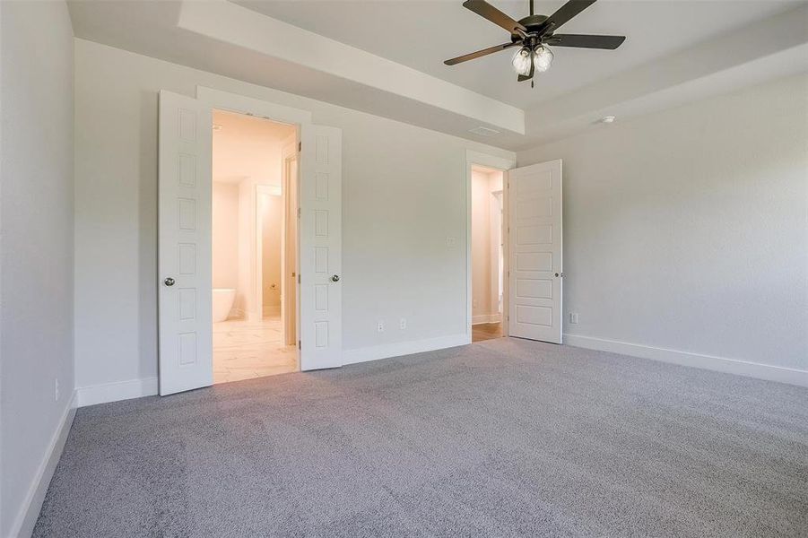 Unfurnished bedroom featuring carpet, a tray ceiling, and ceiling fan