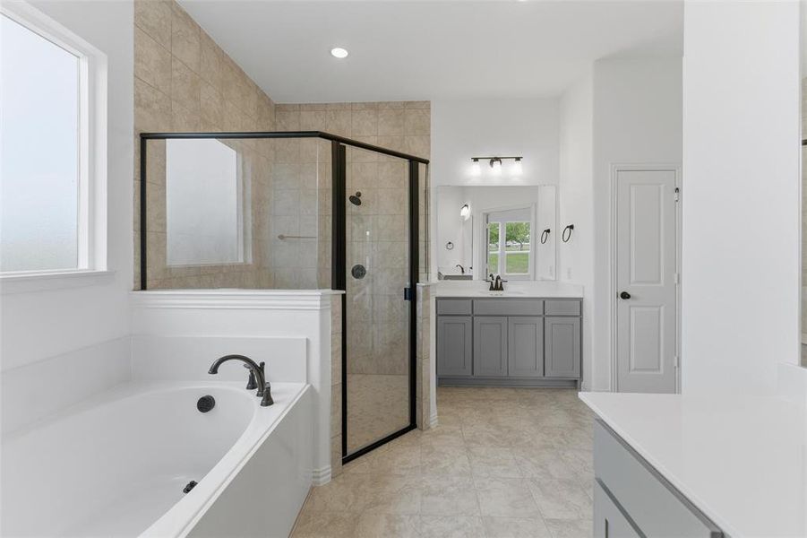 Bathroom featuring a built-in bathtub, a walk-in shower with clear glass, a vanity with gray cabinetry, and tile flooring