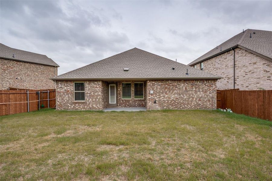 Back of house with a shingled roof, brick siding, a patio area, and a fenced backyard