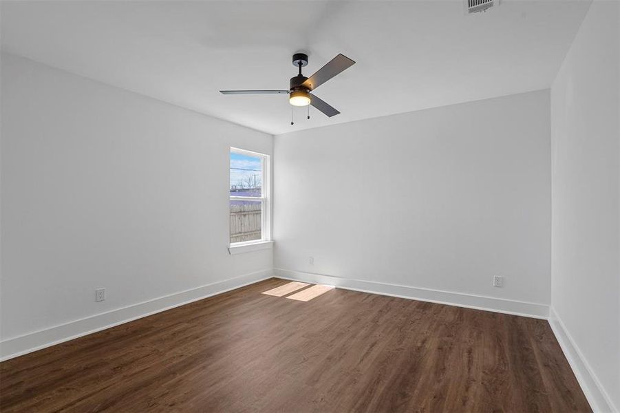 Empty room featuring dark wood finished floors, visible vents, baseboards, and a ceiling fan