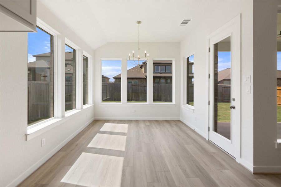 Unfurnished sunroom featuring a chandelier, vaulted ceiling, wood finished floors, and healthy amount of natural light