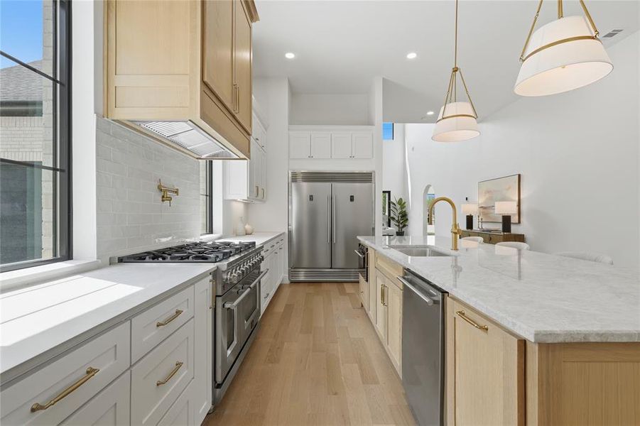 Gourmet kitchen featuring a large island with sink, stainless steel appliances, light wood-finish flooring, white subway tile backsplash, and elegant pendant lighting