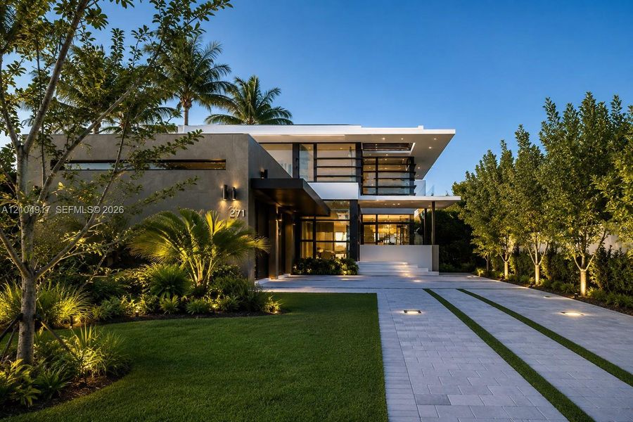 Modern two-story architectural exterior featuring smooth stucco finish, expansive glass windows, integrated landscape lighting, and a paved driveway with linear grass accents